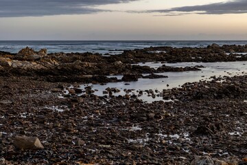 Fototapeta na wymiar Sandy beach, with rocky outcroppings at the shoreline at sunset in Franzkraal, South Africa