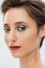 close up view of young model with bright makeup looking at camera isolated on grey.