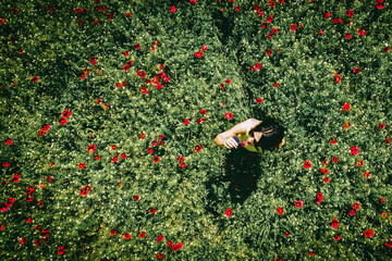 Top aerial girl smell flower in poppy field spring nature. Red green poppy flower field .Concept of...