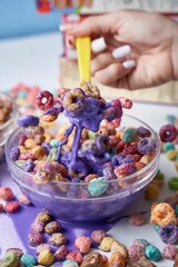 Closeup of a hand taking a spoon of appetizing cereal from a bowl filled with purple milk