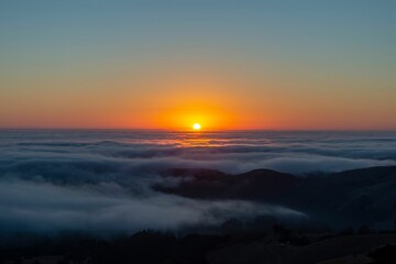 Stunning sunrise over a vast valley with hills and wispy low clouds blanketing the landscape