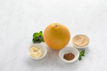 Ingredients for a delicious diet dessert: grapefruit, butter, brown sugar, cinnamon and mint on a light gray background, copy space