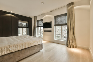 a bedroom with wood flooring and large windows that look out onto the street in front of the apartment building