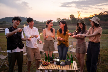 Group of young Asian people are enjoy camping , playing sparkler in natural campsite at twilight