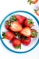 White bowl with fresh chopped strawberries on a white wooden background. Top view.