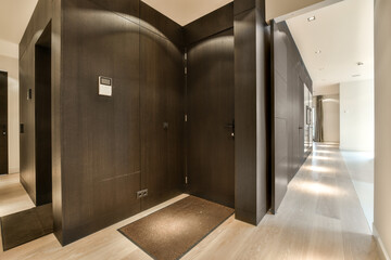 a hallway with wood floors and black wall paneled doors on either side of the room, there is a toilet in the corner