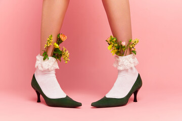 Close up portrait of female feet wearing shoose and white fancy socks with flower inside over pink studio background. Spring fashion