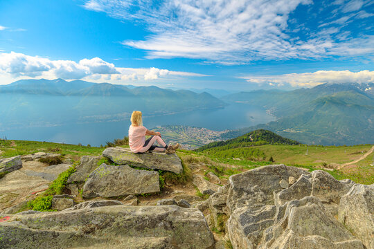relaxing woman taking a break after trekking, sitting on top of Cardada-Cimetta mount in Switzerland. Skyline from Swiss chairlift of Locarno on Cardada mount. Lake Langensee cityscape in Ticino.