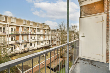 a balcony with buildings in the background and a white door leading to an apartment building that has been boarded up