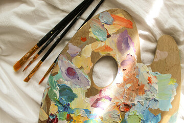 Palette and brushes photo on the white blanket. Art, aesthetic sunny vibe, spring, summer mood.