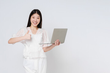 Young asian woman holding a laptop and showing thumbs up isolated on white background.