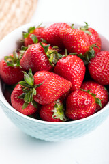 Fresh strawberries in a blue ceramic bowl, on a white table. 