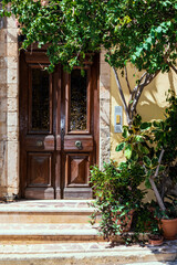 Old shabby wooden door of a Greek house, green tree, stone steps