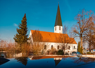 Church on a sunny winter day with reflections on a car roof at Mamming, Dingolfing-Landau, Bavaria,...