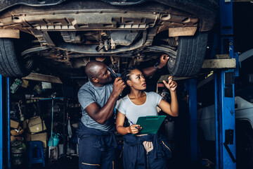 Fototapeta na wymiar Professional Car Mechanic is Investigating Under a Vehicle on a Lift in Service. Auto Service Worker Checking Car Under Carriage Look For Issues. Car service technician check and repair customer car.