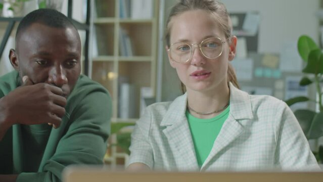 Medium close up shot of gen Z diverse male and female colleagues working on laptop and speaking while cooperating in office