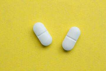 White pills isolated on a yellow background. Top view, flat lay.
