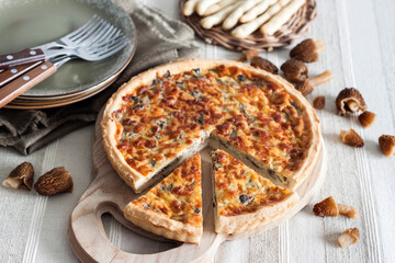 Quiche – open tart pie with morel mushrooms, onion and cheese on wooden cutting board