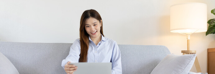 Woman using laptop to work or do homework at home with smiling face in her living room, Creating happiness at work with a smile, Live performance or video call with laptop, Work from home.