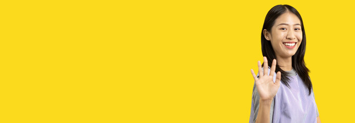 Waving hand in hi, Asian woman smiling friendly greeting, Hello,nice to meet you,say hi, Say hi and greet you, Welcome new people Join a multicultural team, Goodbye, Isolated on yellow background. © Puwasit Inyavileart