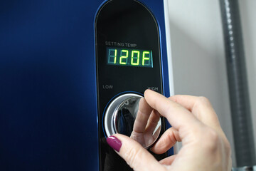 Female hand adjusting a tankless instant hot water heater. Display showing 120°F 