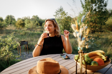 Happy Woman freelancer use phone and drinking cocktail call while relaxing on cozy glamping tent in sunny day. Luxury camping tent for outdoor summer holiday and vacation. Lifestyle concept