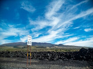 Small speed limit sign with the number 60 printed on it with a green field on a mountain range