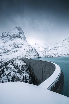 Blue water in Emosson dam in winter with snowy mountains and a dark and moody sky in the background