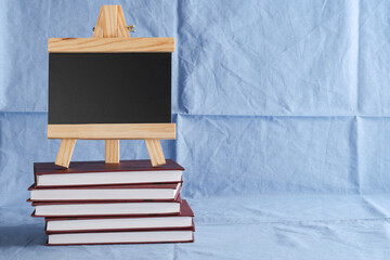 black board for text on stack of books on blue textile background. copy space. Education and exhibitions, meetings concept. Back to school