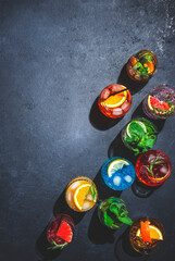 Cocktails set on black bar counter, top view. Mixology concept. Assortment of colorful strong and low alcohol drinks for cocktail party. Dark background, hard light, copy space