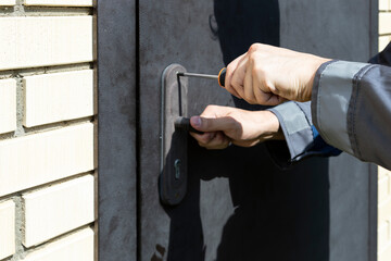 Close up photo of repairman with screwdriver fixing a door on the backyard	