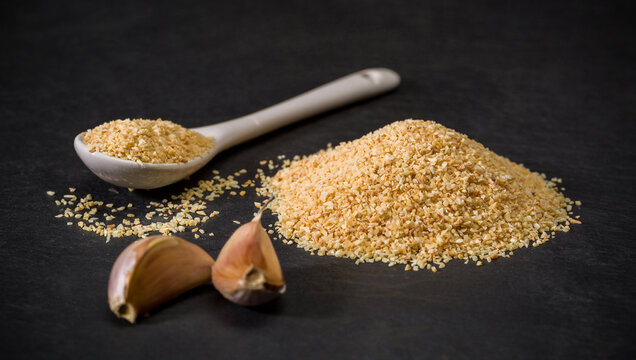 Garlic spice for recipes. Spoon and a pile of garlic powder. Garlic head and cloves on the table.