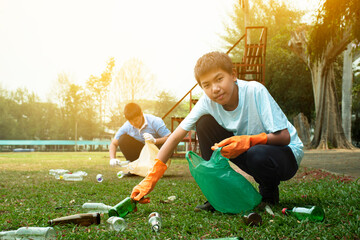 Asian boy in caucasian is clearing and separating garbages with his friend at the park, soft and selective focus, environment care, community service and summer vacation activity of teenagers concept.