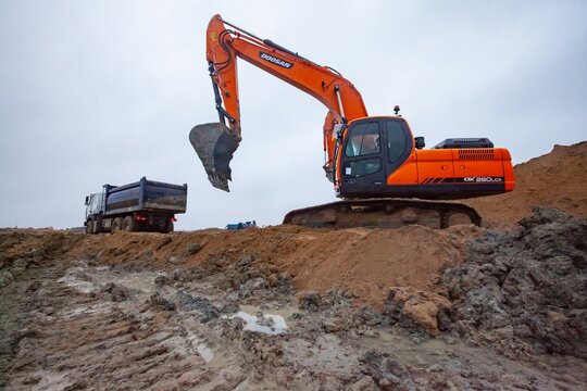 Ust-Luga, Leningrad oblast, Russia - November 16, 2021: Excavators Doosan load truck on construction site. Rainy day, dirty ground.