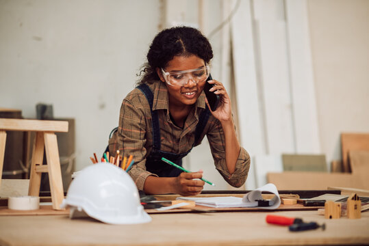 Happy african american woman using smartphone for confirrm order and customer service, Small business owner young black female carpenter working a wood work in carpentry workshop.