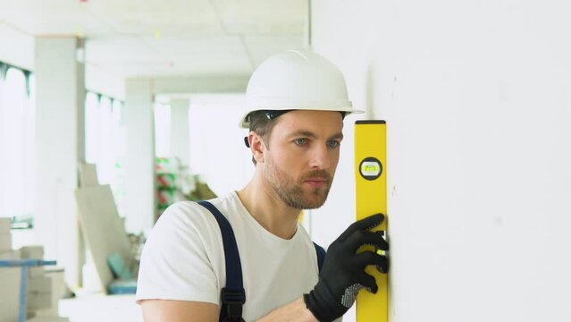 A man builder measures of the vertical deviation of plasterboard wall. Bubble level ruler close up view, measuring and leveling concept