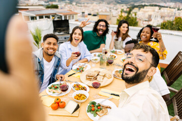 Fototapeta na wymiar Happy young group of multiracial friends enjoying barbecue dinner party at house terrace. Millennial cheerful men and women taking selfie portrait with phone during birthday celebration.