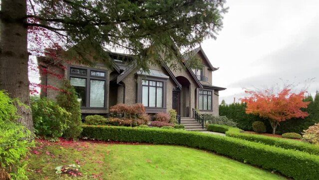 Establishing shot of two story stucco luxury house with garage door, big tree and nice Fall Foliage landscape in Vancouver, Canada, North America. Day time on Sept 2023. ProRes 422 HQ.
