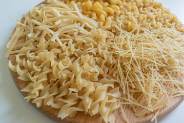 Close up photo of the pasta of different types on a round wooden stand on a white background
