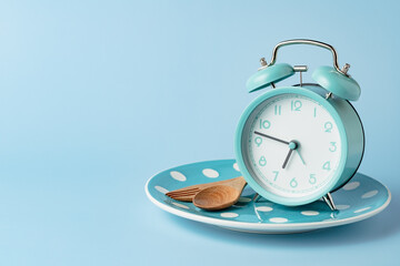 An alarm clock on an empty plate and cutlery set against blue background