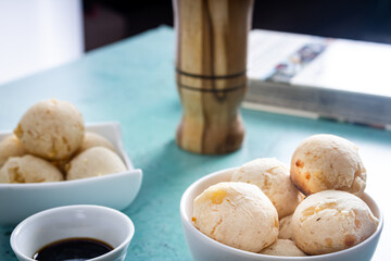 Delicious cheese bread, typical Brazilian dish, on a table with a green background and white wall. Next to a cup of coffee.