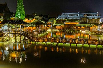 Fototapeta premium Night time view of flat wooden bridge crossing the canal surrounded by traditional Chinese houses in the historic scenic Wuzhen water town, China