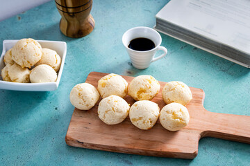 Delicious cheese bread, typical Brazilian dish, on a wooden board and table with a green background and white wall. Next to a cup of coffee.