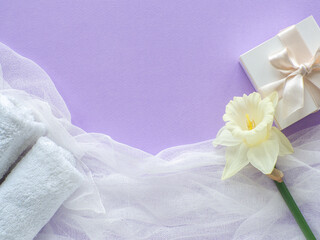 Daffodils flower, towels and gift box with copy space on lilac background. Women and Mothers Day gift. Concept of wellness, SPA and relaxation. Congratulations note and towels violet flat lay.