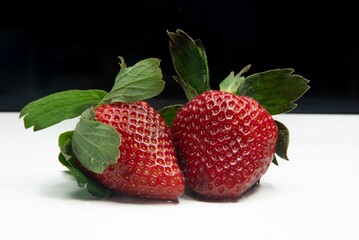 Ripe, large strawberries with fresh green leaves sit side by side on a white background