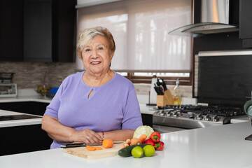 Happy grandmother in her kitchen - elderly woman cooking healthy food in her kitchen