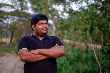 South asian overweight young man standing within green natural environment