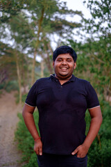 South asian overweight young man standing within green natural environment