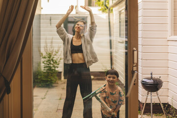 Happy family washes the window. Mom and son do house cleaning. Boy using a squeegee to wash a...