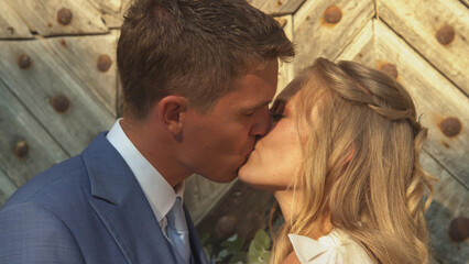 CLOSE UP: Romantic newlyweds sharing a loving kiss in front of wooden gates